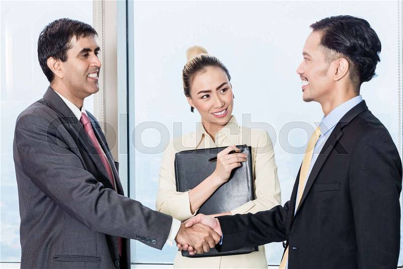 Asian secretary introduces applicant to boss for job interview and they shake hands in office, stock photo