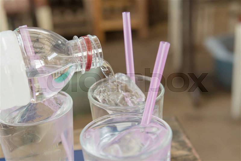 Water pouring on a plain glass with ice and pink straw. Selective focus, stock photo