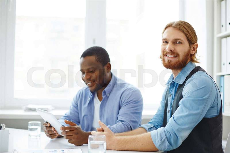 Smiling young businessman sitting at the table with his colleague, stock photo