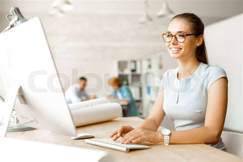 Young designer sitting in front of computer monitor in office, stock photo
