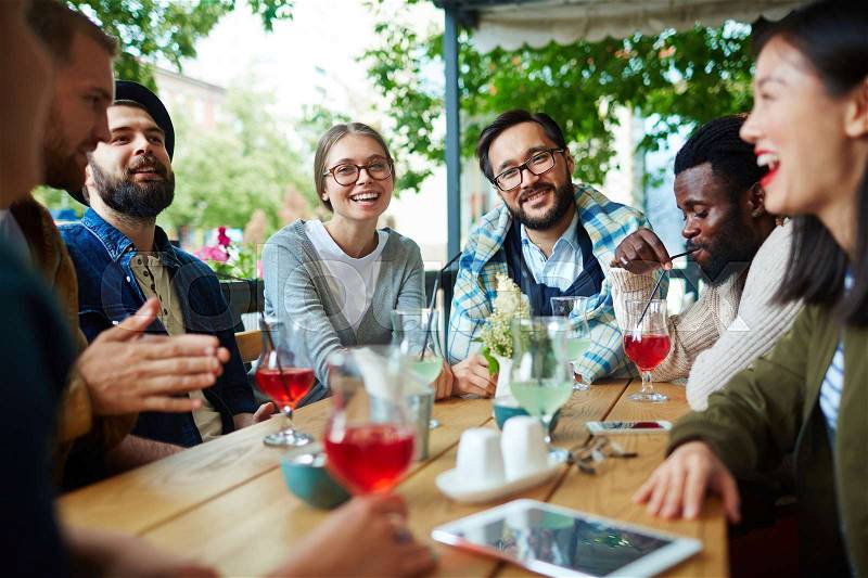 Happy young people having friendly conversation in summer cafe, stock photo