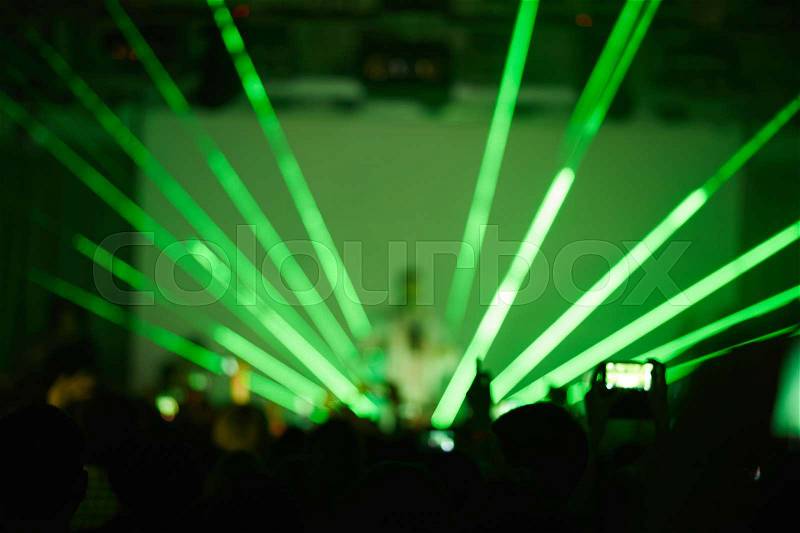 Defocused image of crowd enjoying performance and musician on stage in bright green rays of strobe lights, stock photo