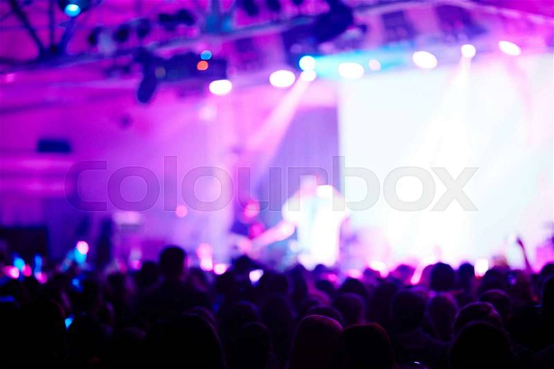 Blurred image of performer on purple-lit stage before large crowd of fans admiring his music, stock photo