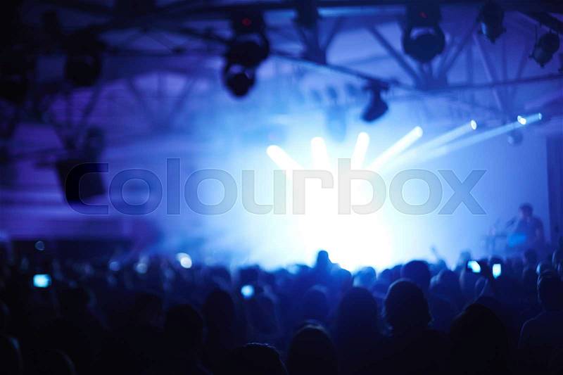 Large crowd of fans dancing before big bright stage enjoying music of young band, defocused image, stock photo