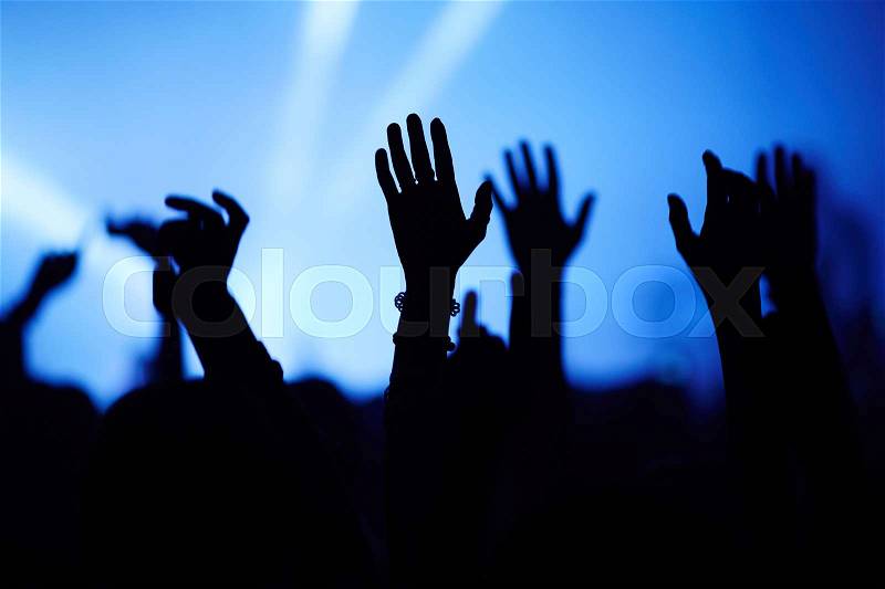 Silhouettes of people at concert with hands raised, stock photo