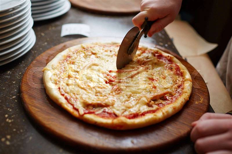 Close-up of cook cutting pizza with pizza cutter, stock photo