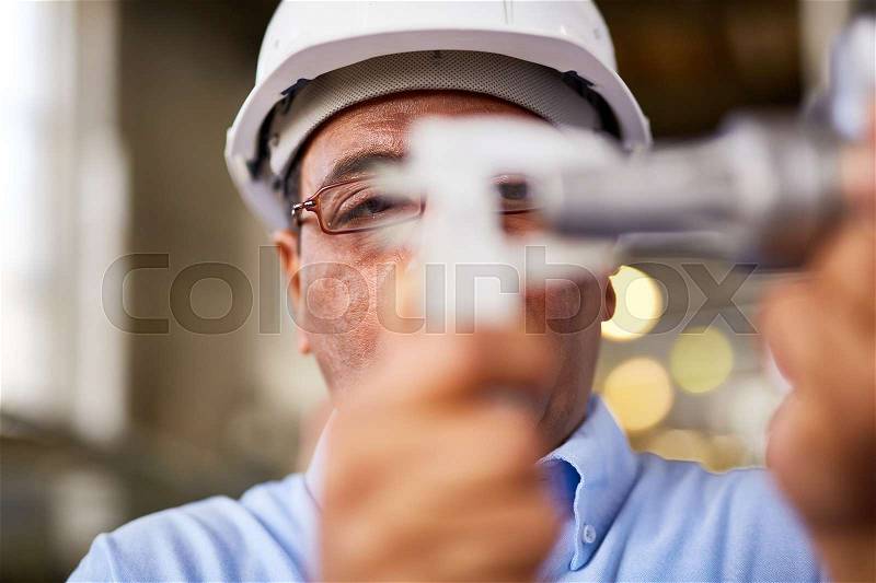 Serious manual worker in eyeglasses measuring detail, stock photo