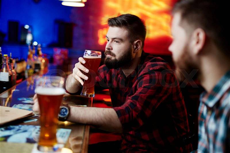 Pensive man sitting at bar counter and drinknig beer, stock photo