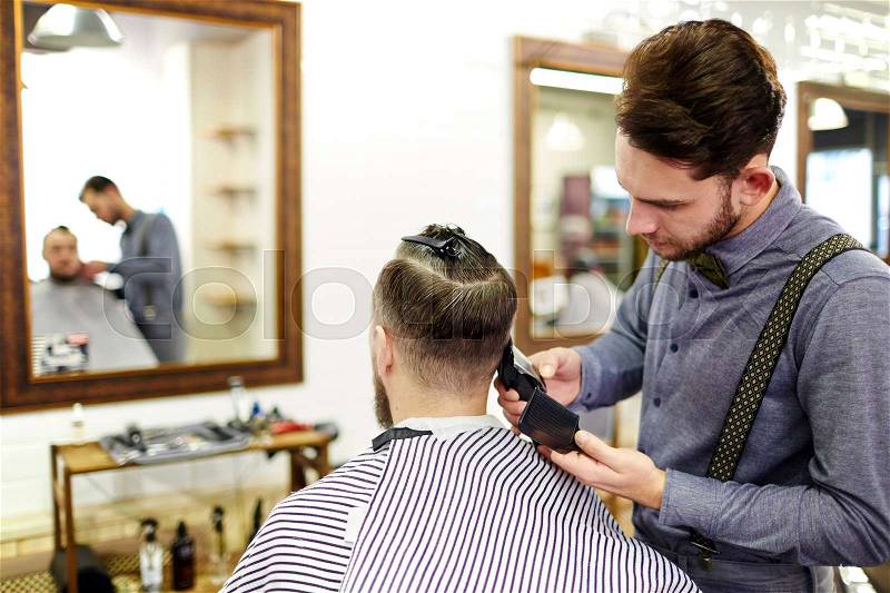 Barber cutting hair with electric razor at a barbershop, stock photo