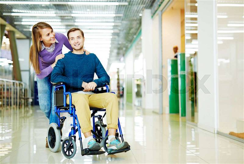 Full color image of young couple, handicapped man in wheelchair and his girlfriend, enjoying leisure time at shopping center together, stock photo