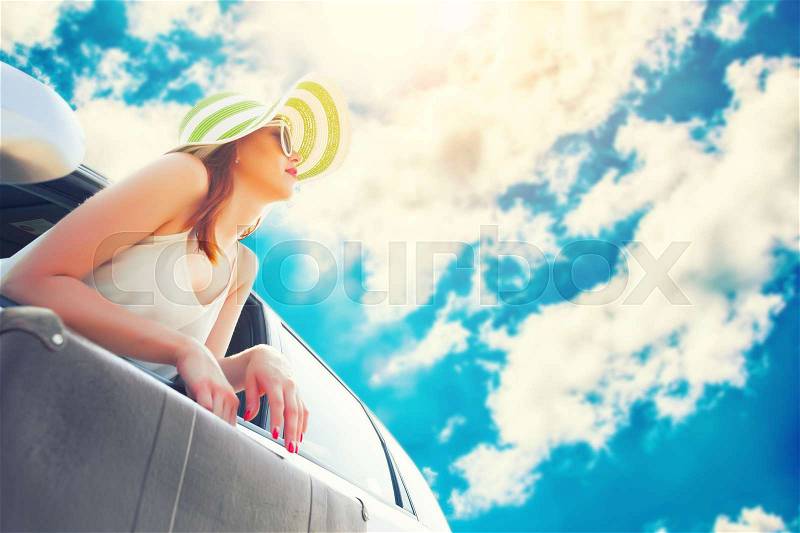 Happy woman looks out the car window with suitcase in hands, stock photo