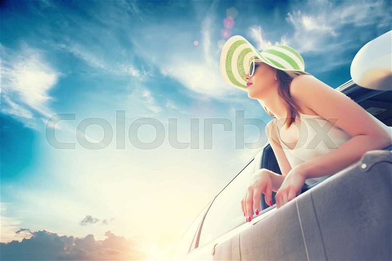 Happy woman looks out the car window with suitcase in hands, stock photo