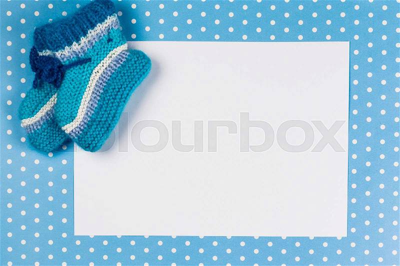 Knitted baby socks and blank note on blue polka dot background, stock photo
