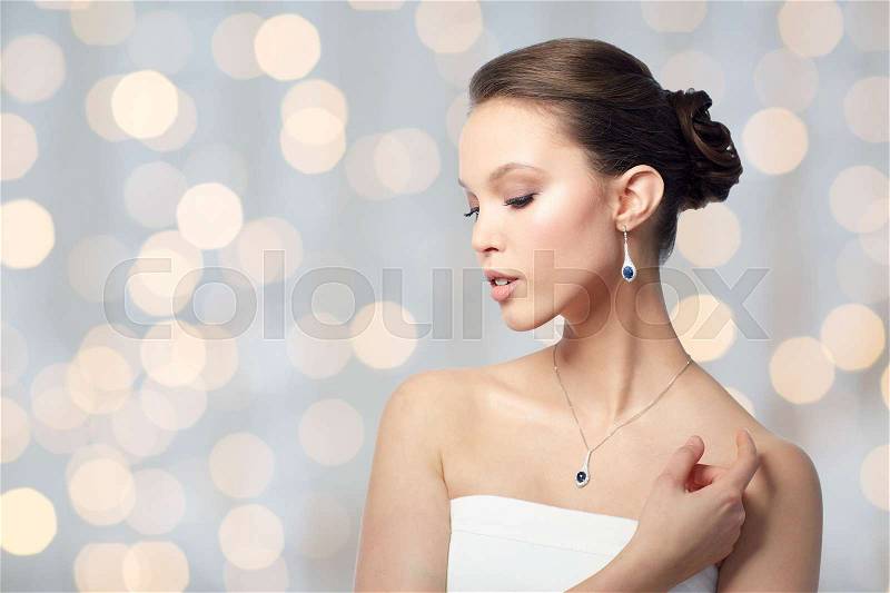 Beauty, jewelry, wedding accessories, people and luxury concept - beautiful asian woman or bride with earring and pendant over holidays lights background, stock photo