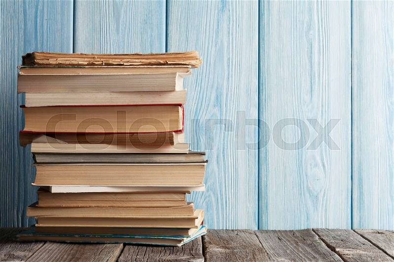 Stack of books on table in front of wooden wall. With copy space, stock photo