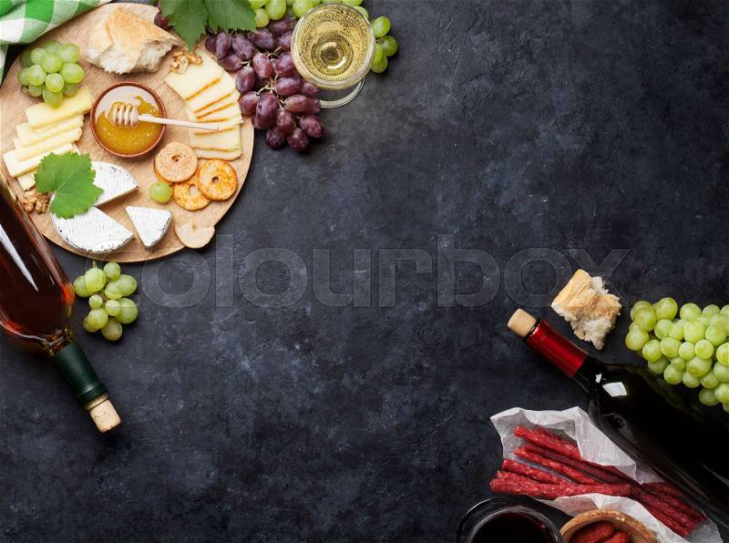 Red and white wine bottles, grape, cheese and sausages over stone table. Top view with copy space, stock photo