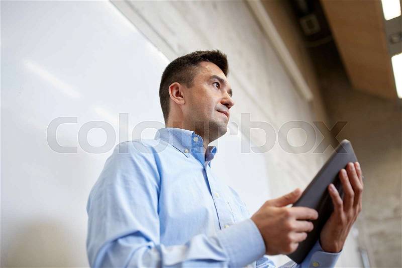 Education, school, business, technology and people concept - teacher or businessman with tablet pc computer standing at white board at lecture hall, stock photo