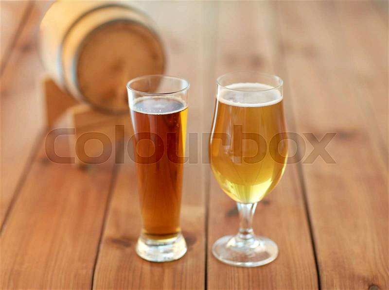 Brewery, drinks and alcohol concept - close up of different beers in glasses and barrel on wooden table, stock photo