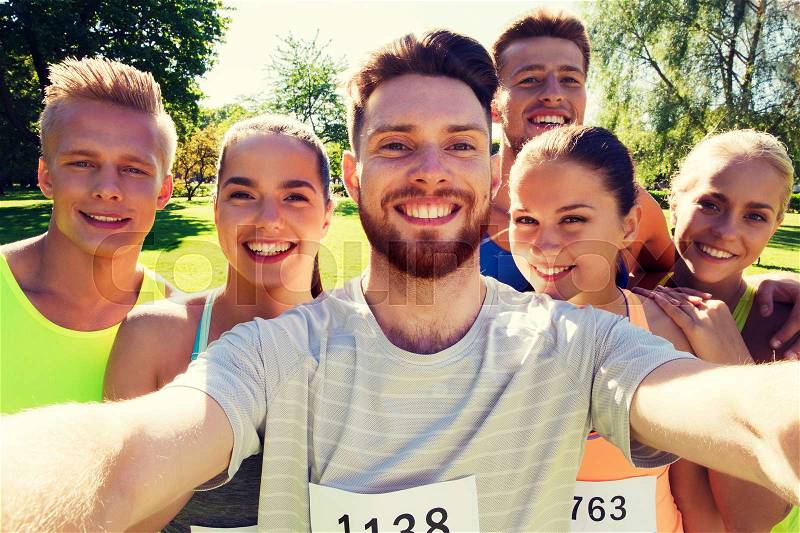 Fitness, sport, friendship, technology and healthy lifestyle concept - group of happy teenage friends with racing badge numbers taking selfie by smartphone at marathon outdoors, stock photo