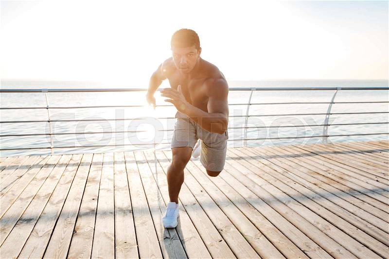 Focused african american young sportsman is ready to start running on pier, stock photo