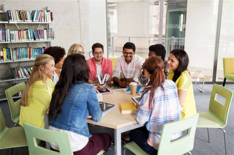 Education, high school, learning, people and technology concept - group of international students sitting at table with tablet pc computers and books and talking at university, stock photo
