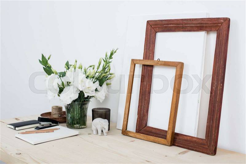 White contemporary feminine work desk with flowers, art frames and notepad, home office interior closeup, stock photo