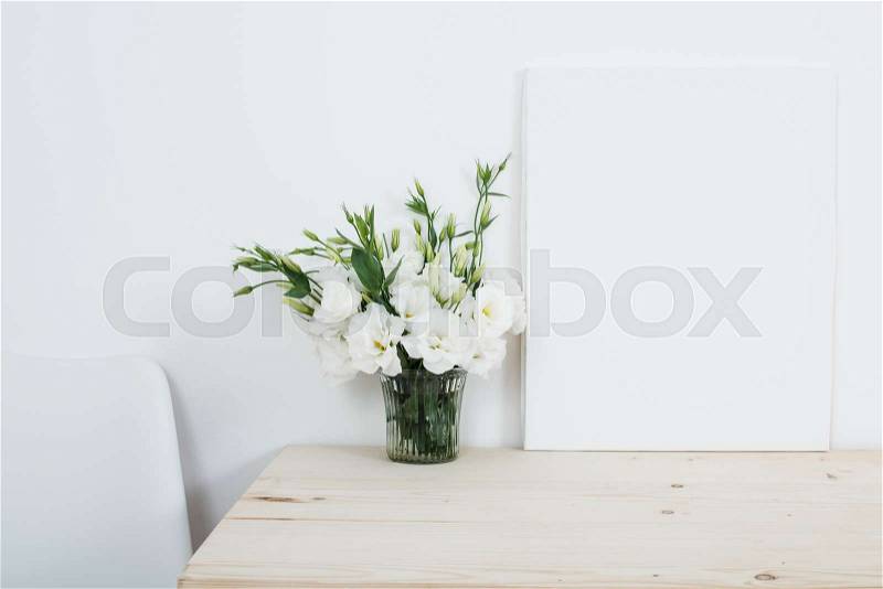 White interior decor, fresh natural flowers in vase and empty canvas on table, stock photo
