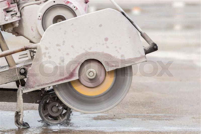A worker cutting concrete road with diamond saw blade machine, stock photo