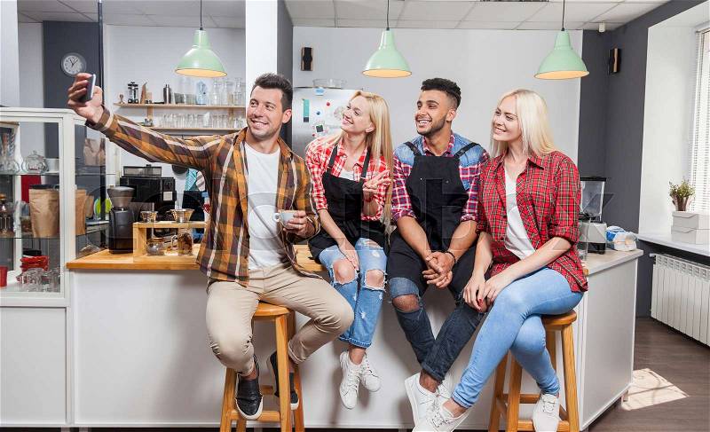 People taking selfie friends pictures drinking coffee shop with barista sitting at bar counter, mix race men hold smart phone woman happy smile, stock photo