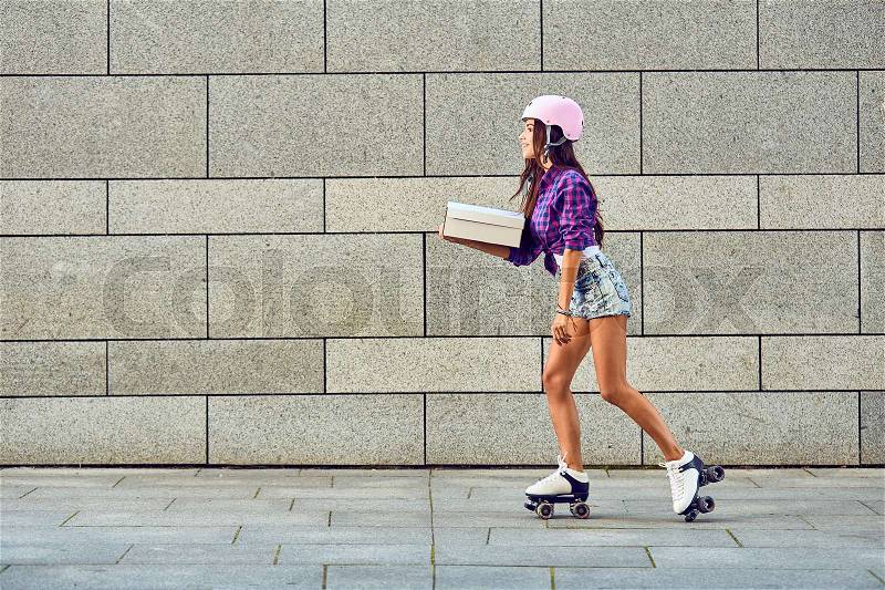 Fast delivery of sportive girl on roller skates. Young woman on roller skates with box or pizza in hands, stock photo