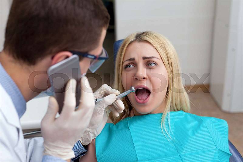 Dentist working with woman and speaking on the phone, woman is scared, stock photo