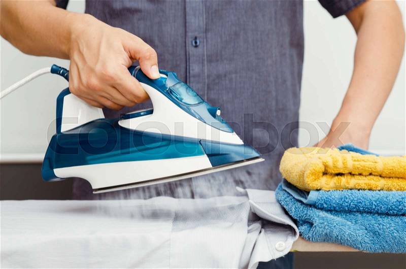 Man irons clothes on ironing board with blue steaming iron, stock photo