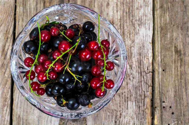 Black and Red Currant in Crystal Bowl on Rustic Wooden Background, stock photo