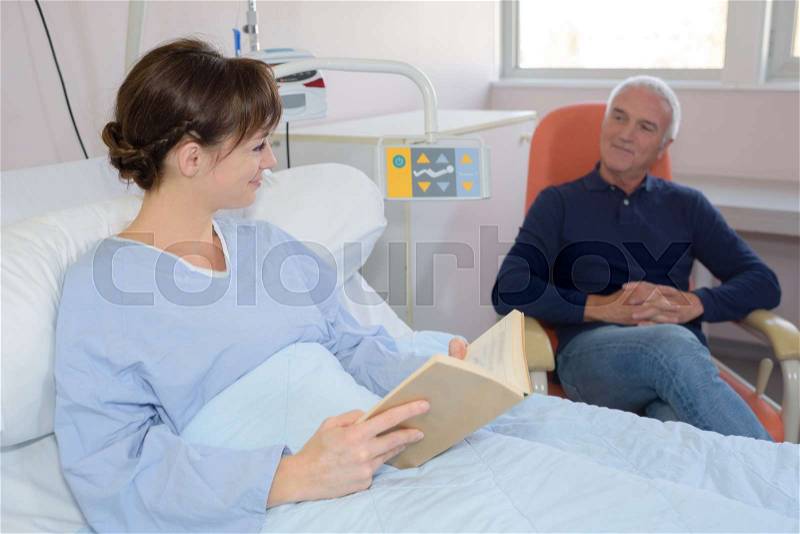 Female patient in bed, relative sat in chair, stock photo