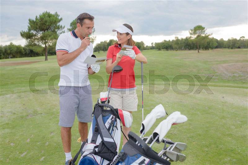 Couple on golf course holding leaflet, stock photo