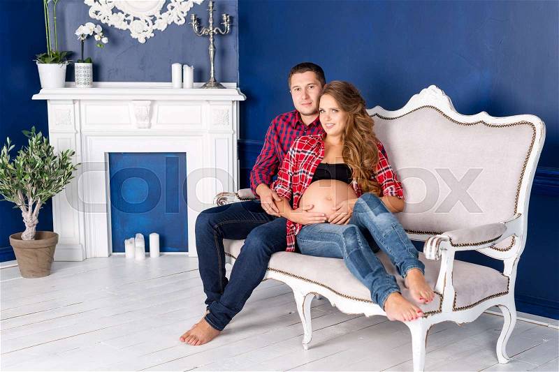 Beautiful pregnant couple relaxing on sofa at home together. Happy family, man and woman expecting a child, stock photo