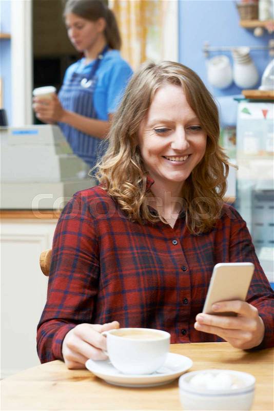 Woman In Coffee Shop Reading Text Message On Mobile Phone, stock photo