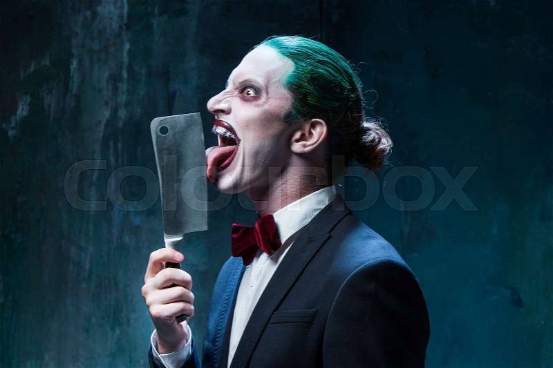 Bloody Halloween theme: The crazy joker face on black background with knife, stock photo