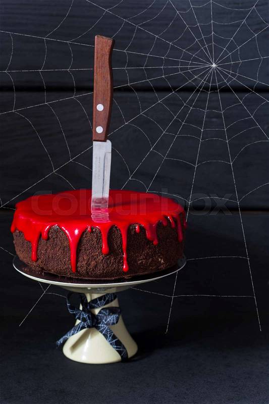 Bleeding monster cake with knife on cakestand and spider web, stock photo