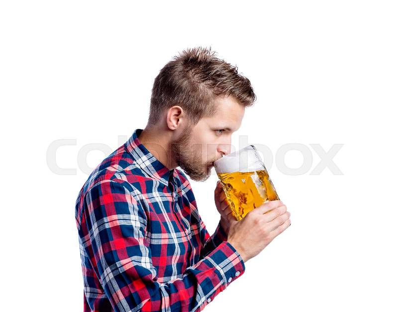 Handsome young hipster man in checked shirt holding a mug of beer, drinking from it. Oktoberfest. Studio shot on white background, isolated, stock photo