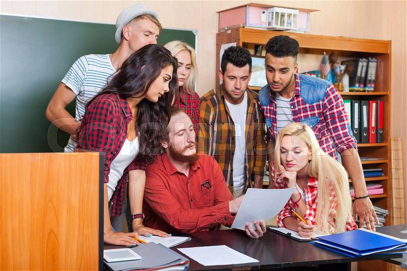 Student High School Group Looking At Paper Document With Professor Sitting At Desk, Young People Teacher Discuss Communicate University Classroom, stock photo