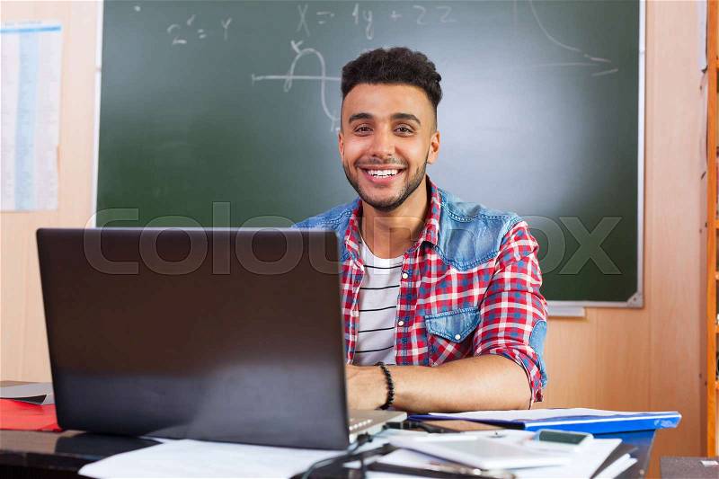 Hispanic Man Using Laptop Computer, Student In University Classroom At Desk Over Chalk Board Happy Smiling, stock photo