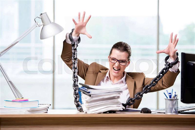 Woman chained to her working desk, stock photo