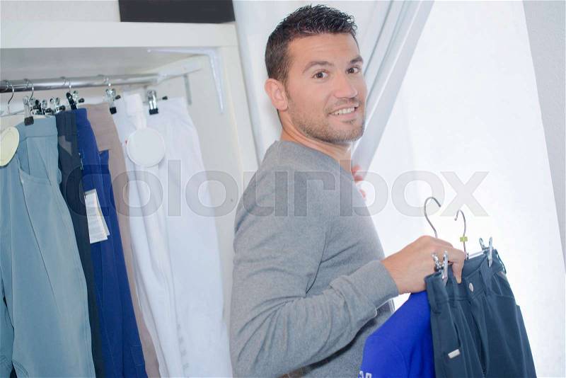 Man entering changing room with selection of clothes, stock photo