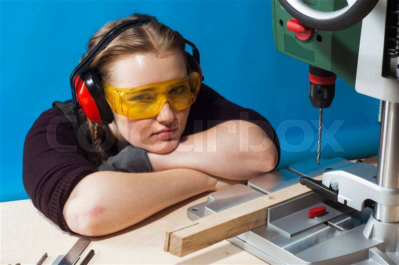 Beautiful female carpenter at work using vertical drilling machine. Photo on blue background, stock photo