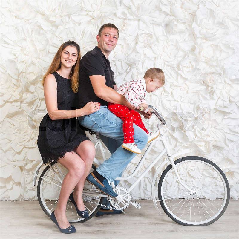 Happy young family with baby boy posing on retro bicycle at studio, stock photo