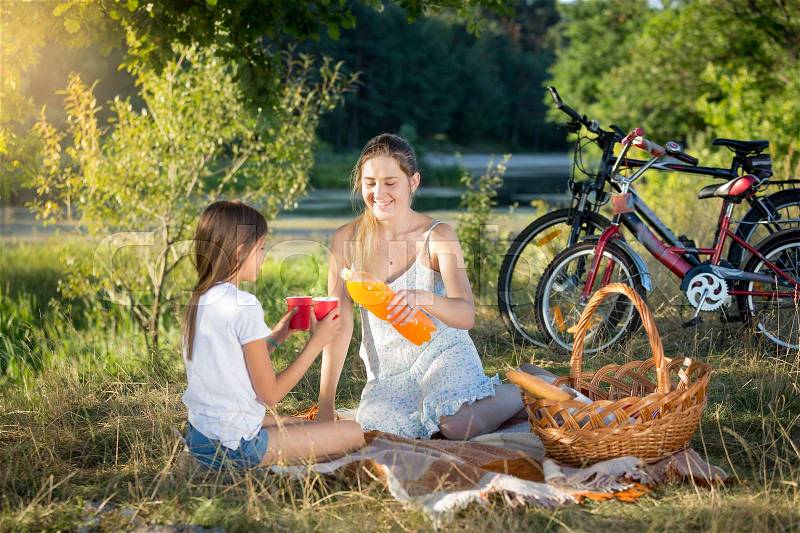 Happy smiling mother and daughter drinking orange juice at picnic, stock photo