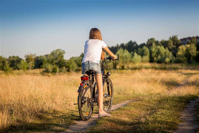 Beautiful girl in shorts and t-shirt cycling in meadow at sunset, stock photo