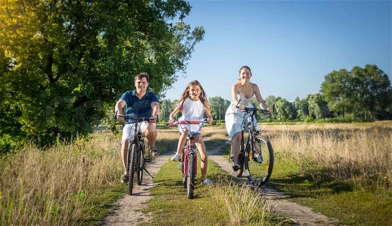 Cheerful young family riding on bicycles at meadow. Concept of family sport, stock photo