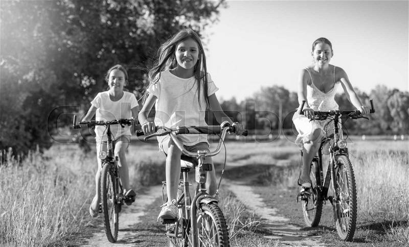 Black and white image of happy young mother riding on bicycles with two daughters, stock photo